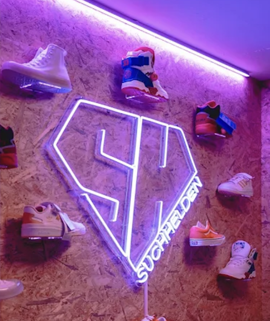 Suchhelden Huddle-Room mit Neon-SH-Diamant und Sneaker-Wall — Brand-Eckraum Suchhelden Huddle-Room mit großem Neon-SH-Diamant und Sneaker-Wall