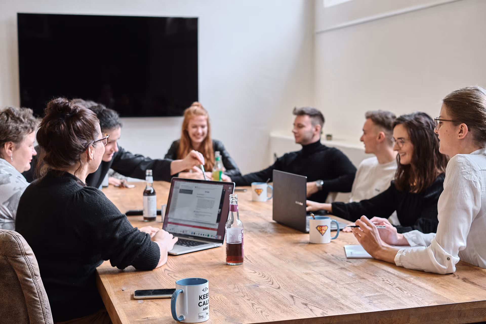 Suchhelden Team-Meeting an einem langen Holztisch mit acht Personen, Laptops und SH-Tassen im Osnabrücker Büro