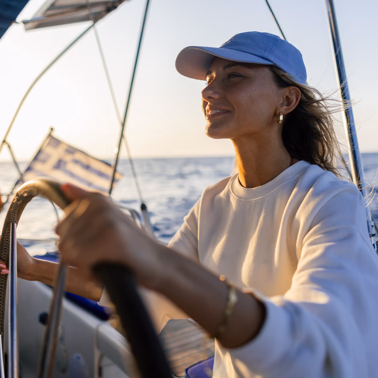 Frau in weißem Pullover und Cap am Steuerrad eines Segelbootes von 1a Yachtcharter im Abendlicht
