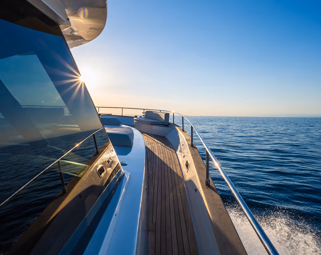 Bug einer Luxusyacht mit Holzdeck und Edelstahlreling auf ruhigem Meer im Sonnenaufgang