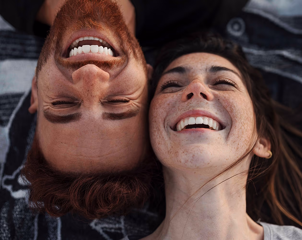 Mann und Frau liegen nebeneinander auf dem Boden und lachen — Sinnbild für gesunden Alltag und Vertrauen in die Marke