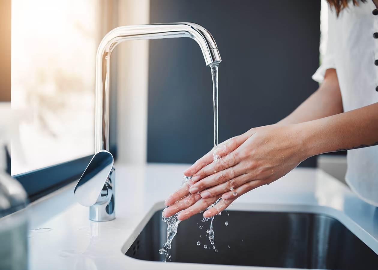 Frau wäscht sich die Hände in der Küchenspüle — Trinkwasser-Alltag, der durch Wavin-Systeme erst funktioniert