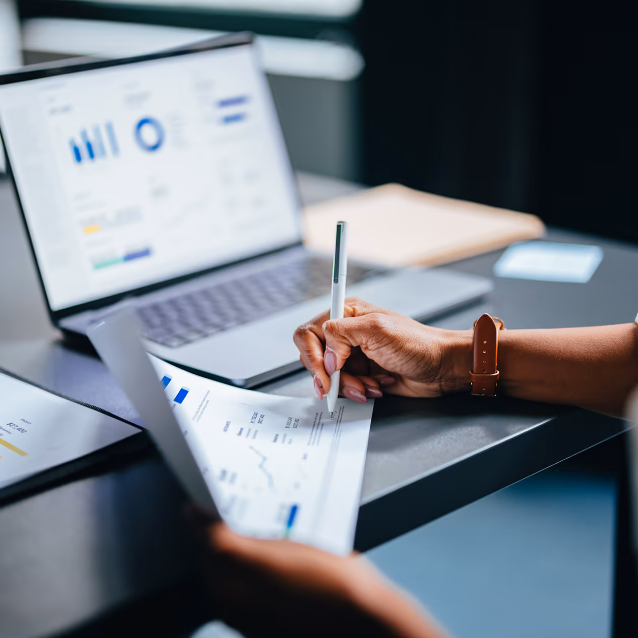 Nahaufnahme: Hände einer Frau, die in einem Büro Charts und Reports analysieren — Sinnbild für die SEO-Audit- und Analyse-Phase
